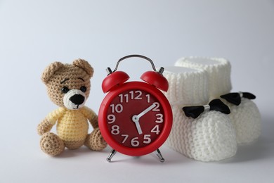 Photo of Alarm clock, toy bear and baby booties on white background. Time to give birth