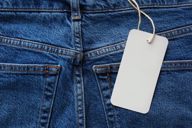 Photo of Cardboard tag with space for text on blue jeans, top view