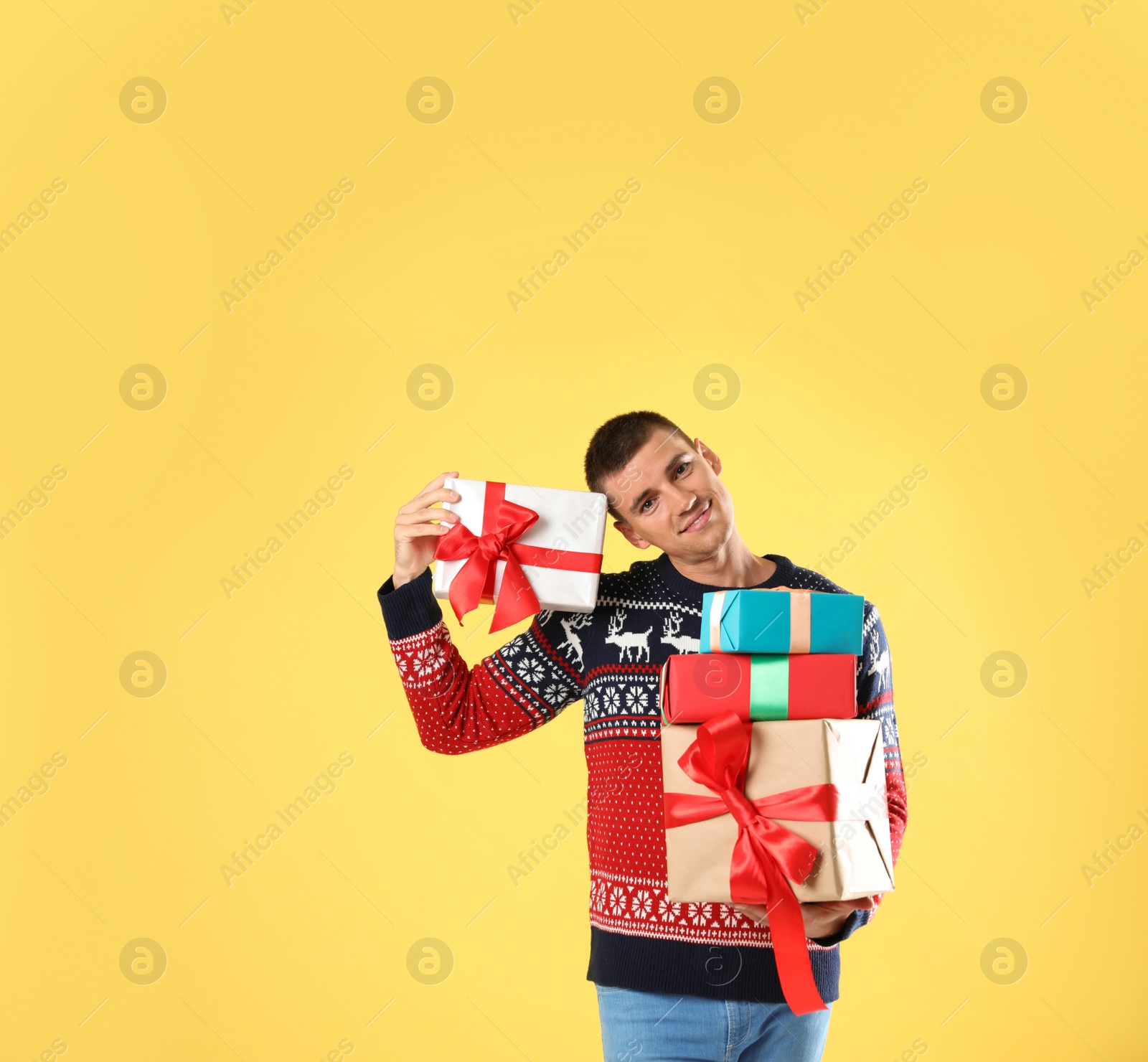 Photo of Happy man in Christmas sweater holding gift boxes on yellow background