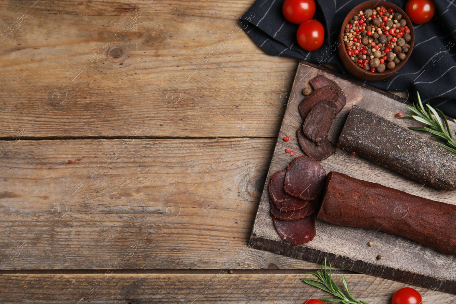 Photo of Delicious dry-cured beef basturma with rosemary and tomatoes on wooden table, flat lay. Space for text