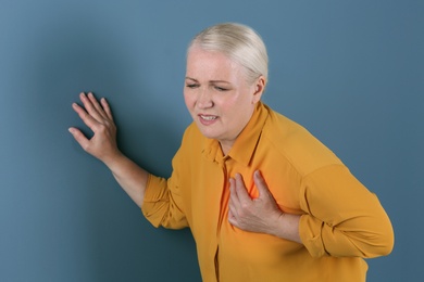 Mature woman having heart attack on color background