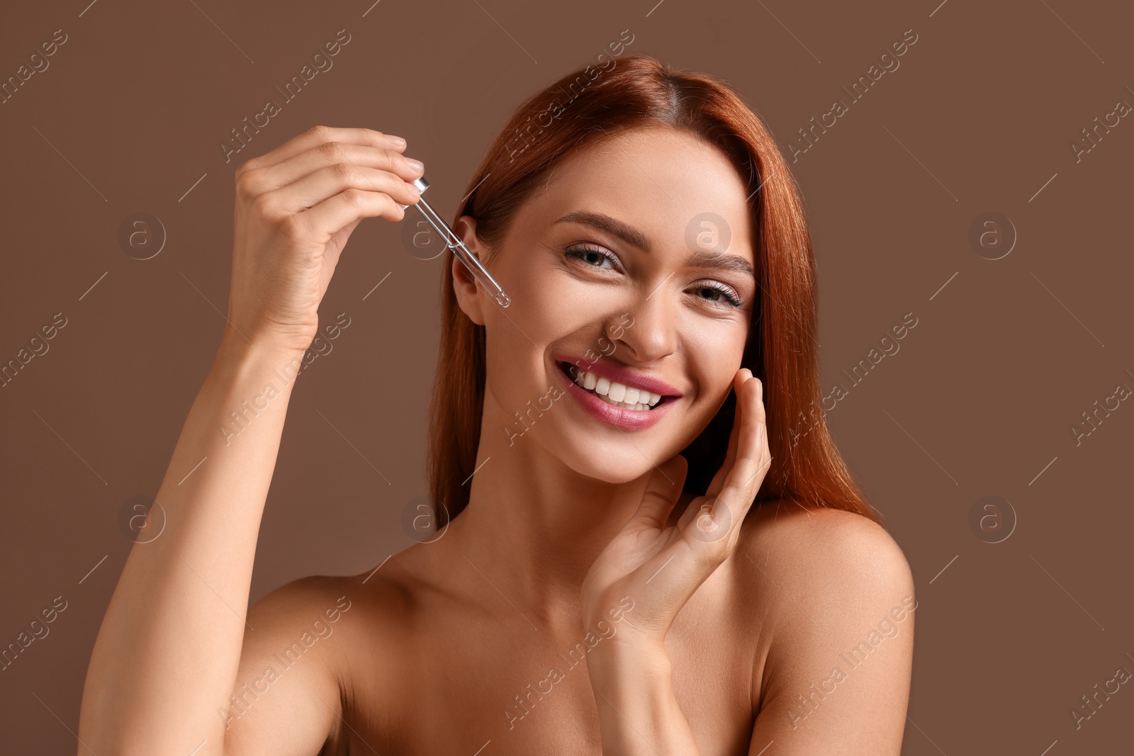 Photo of Beautiful young woman applying cosmetic serum onto her face on brown background