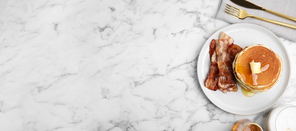 Delicious pancakes with maple syrup, butter and fried bacon on white marble table, flat lay with space for text. Banner design