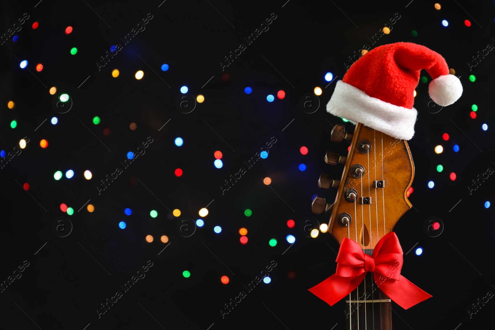 Photo of Guitar with Santa hat and bow against blurred lights. Christmas music concept