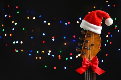 Guitar with Santa hat and bow against blurred lights. Christmas music concept