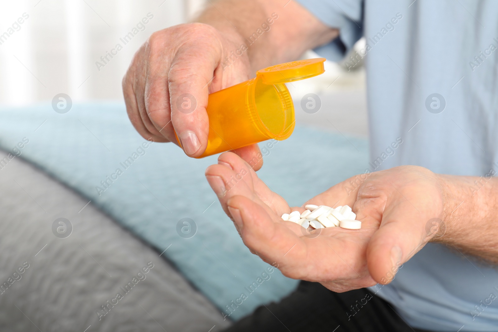 Photo of Senior man pouring pills from bottle into hand indoors, closeup