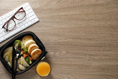 Container of tasty food, keyboard, cutlery and glasses on wooden table, flat lay with space for text. Business lunch