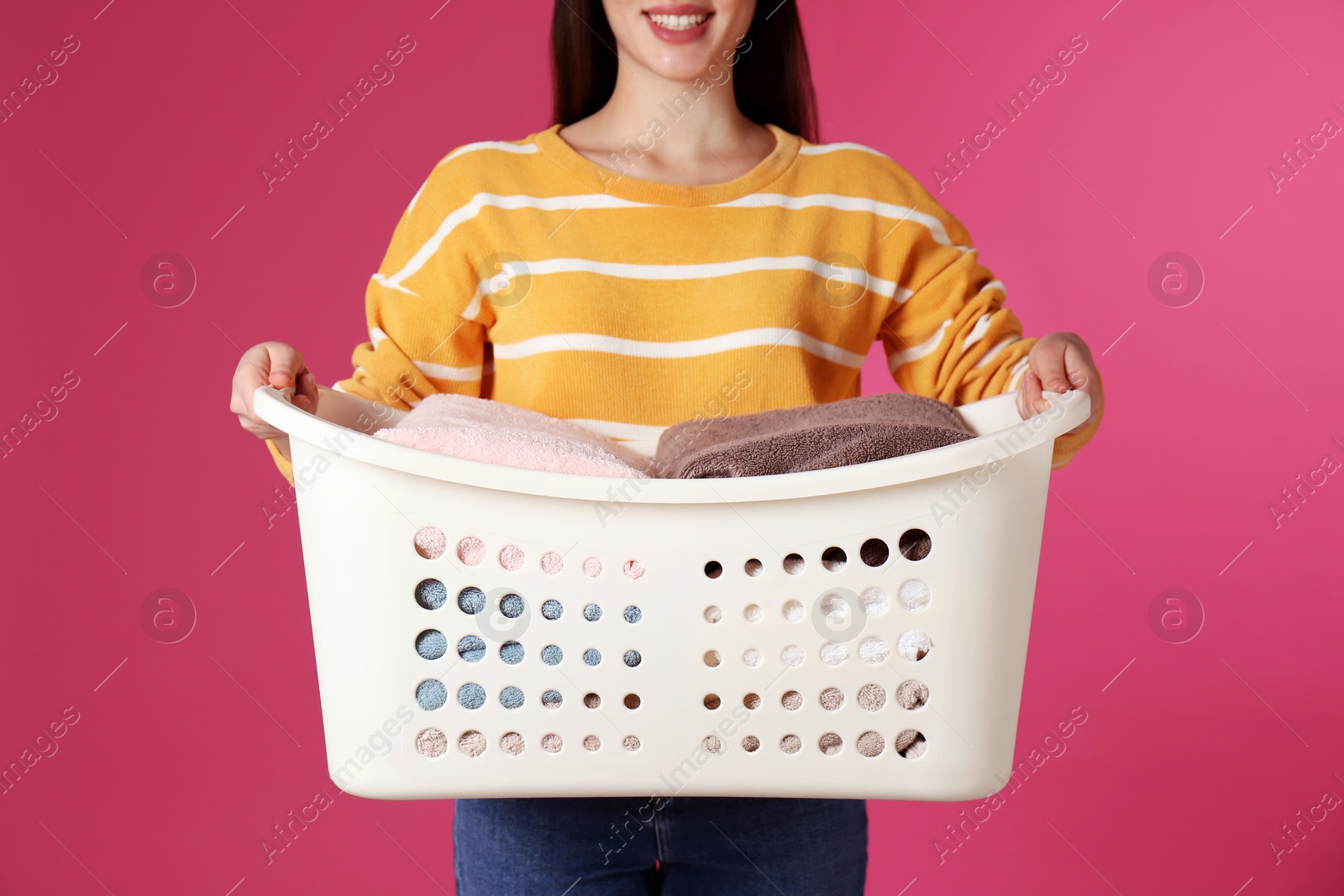 Photo of Young woman holding basket with laundry on color background, closeup