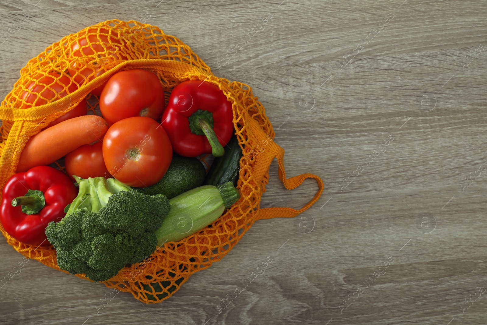 Photo of Net bag with vegetables on wooden table, top view. Space for text