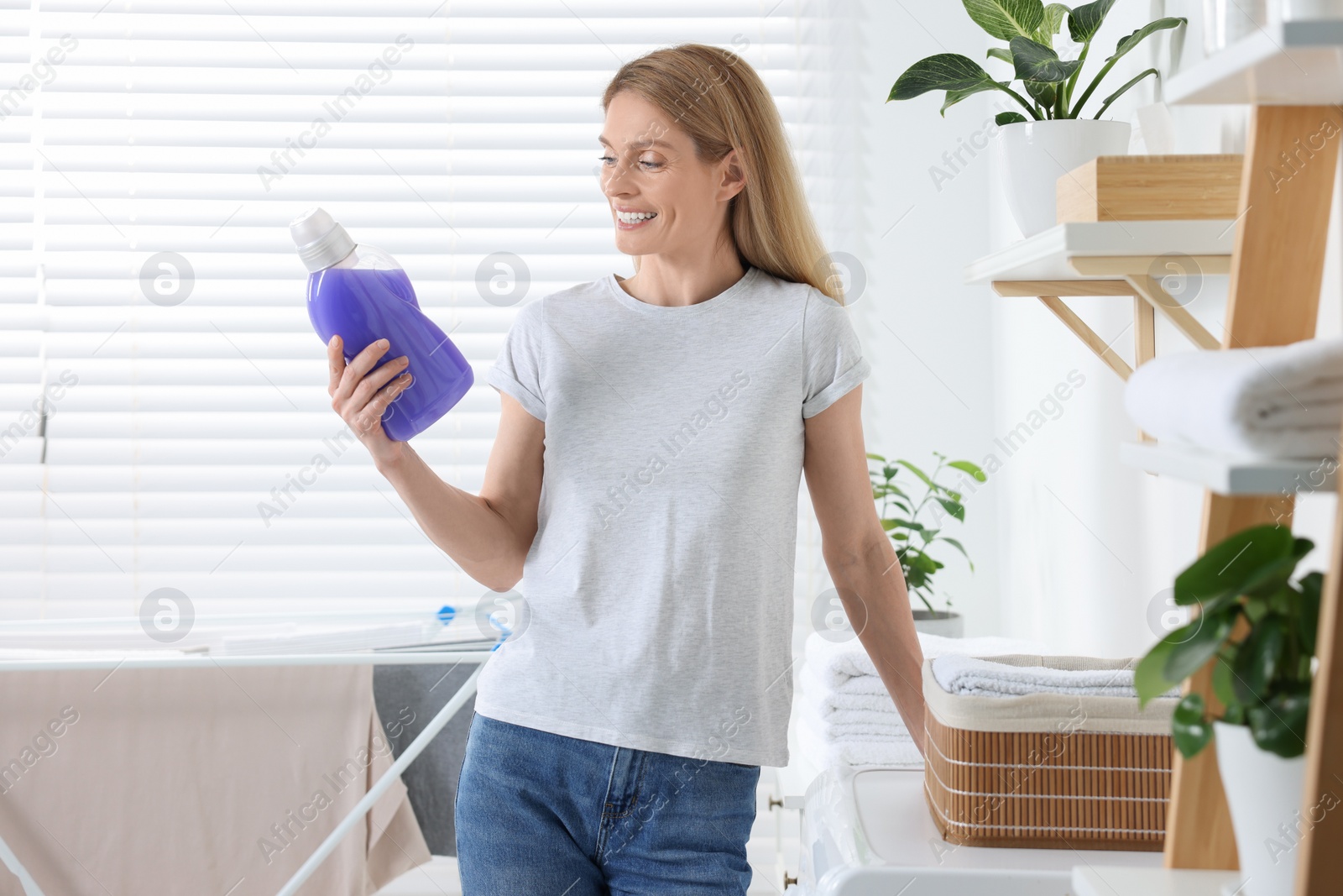 Photo of Beautiful woman holding fabric softener in bathroom