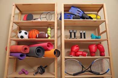Shelving unit with different sports equipment near beige wall indoors