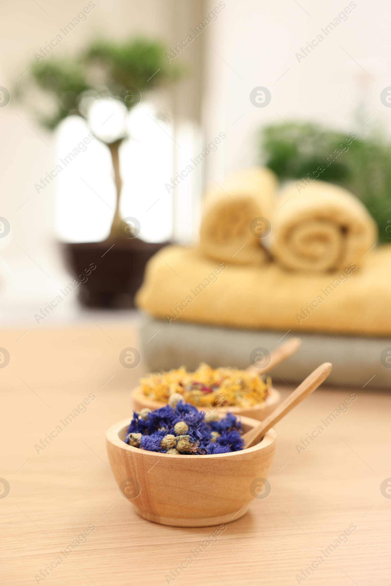 Photo of Bowls with dry flowers and spoons on light wooden table, space for text. Spa therapy