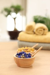 Bowls with dry flowers and spoons on light wooden table, space for text. Spa therapy