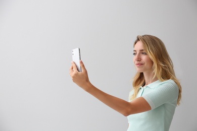 Photo of Young woman unlocking smartphone with facial scanner on grey background. Biometric verification