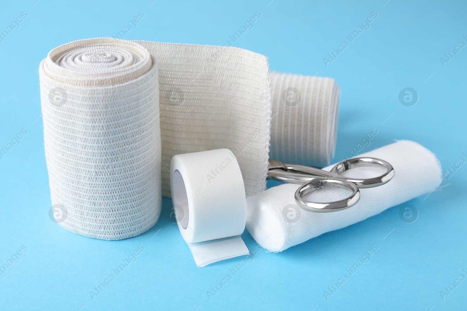 Photo of Medical bandage rolls, sticking plaster and scissors on light blue background