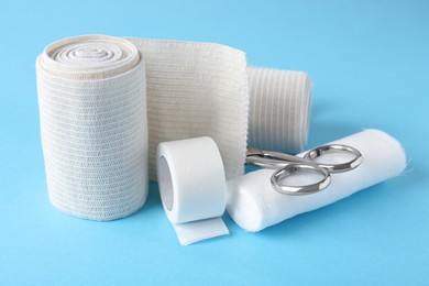 Photo of Medical bandage rolls, sticking plaster and scissors on light blue background