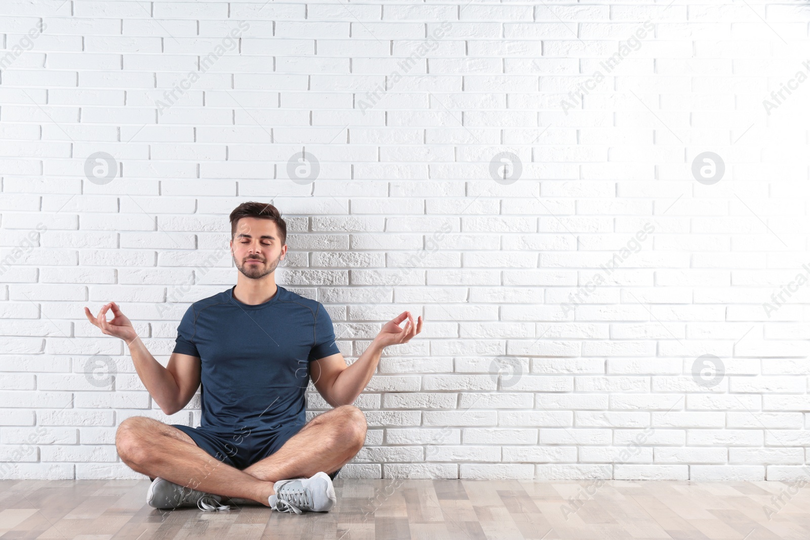 Photo of Handsome young man sitting on floor and practicing zen yoga near brick wall, space for text