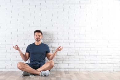 Photo of Handsome young man sitting on floor and practicing zen yoga near brick wall, space for text
