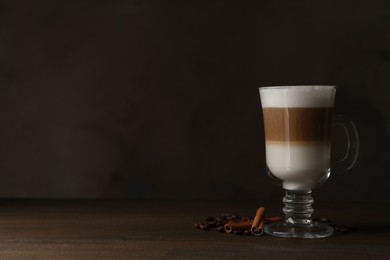 Photo of Hot coffee with milk in glass cup, beans and cinnamon sticks on wooden table. Space for text