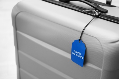 Photo of Grey suitcase with TRAVEL INSURANCE label on blurred background, closeup