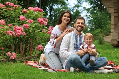 Photo of Happy family in Ukrainian national clothes on green grass outdoors