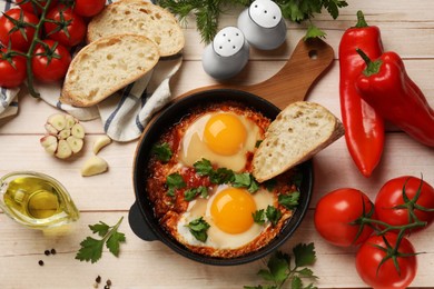 Photo of Flat lay composition with delicious shakshuka in frying pan on light wooden table