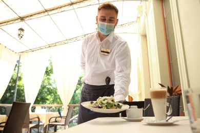 Photo of Waiter serving salad in restaurant. Catering during coronavirus quarantine