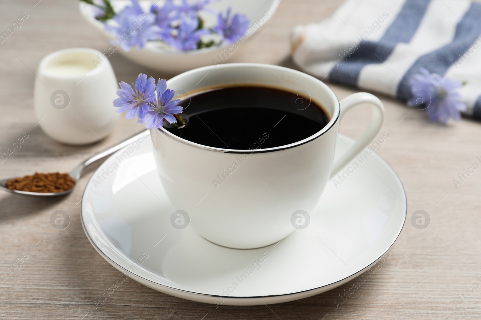 Photo of Cup of delicious chicory drink and flowers on light wooden table