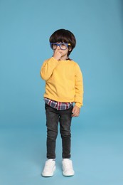 Cute little boy with funny glasses on light blue background