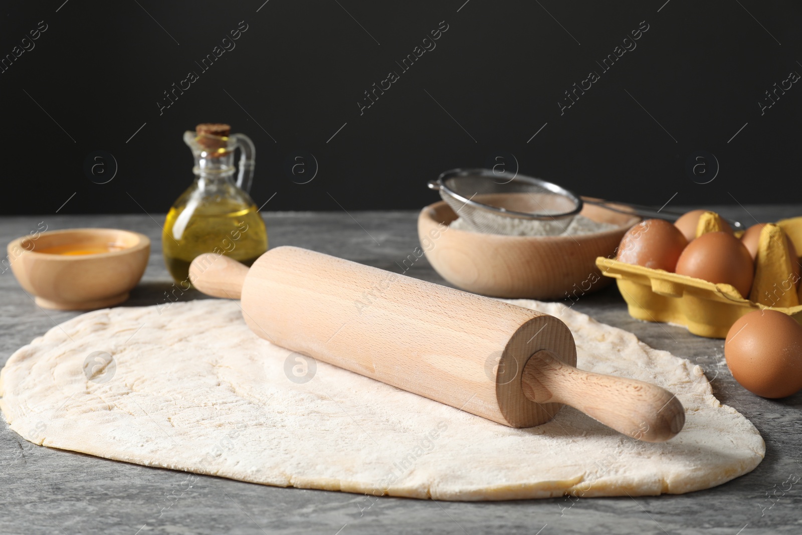 Photo of Raw dough, rolling pin and ingredients on grey table