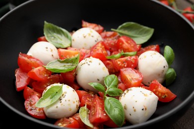 Tasty salad Caprese with tomatoes, mozzarella balls and basil in bowl, closeup