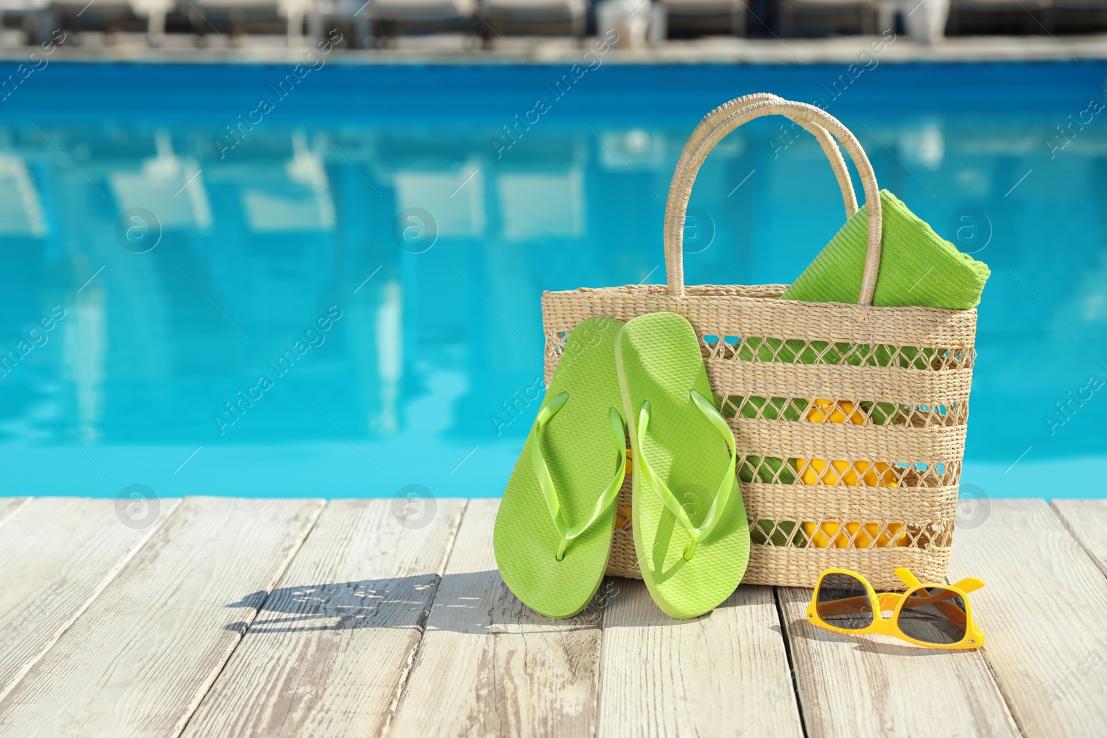 Photo of Beach accessories on wooden deck near outdoor swimming pool, space for text