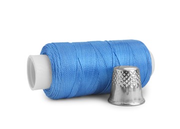Photo of Thimble and spool of light blue sewing thread isolated on white