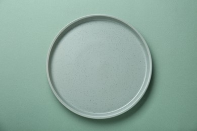 Empty ceramic plate on green background, top view