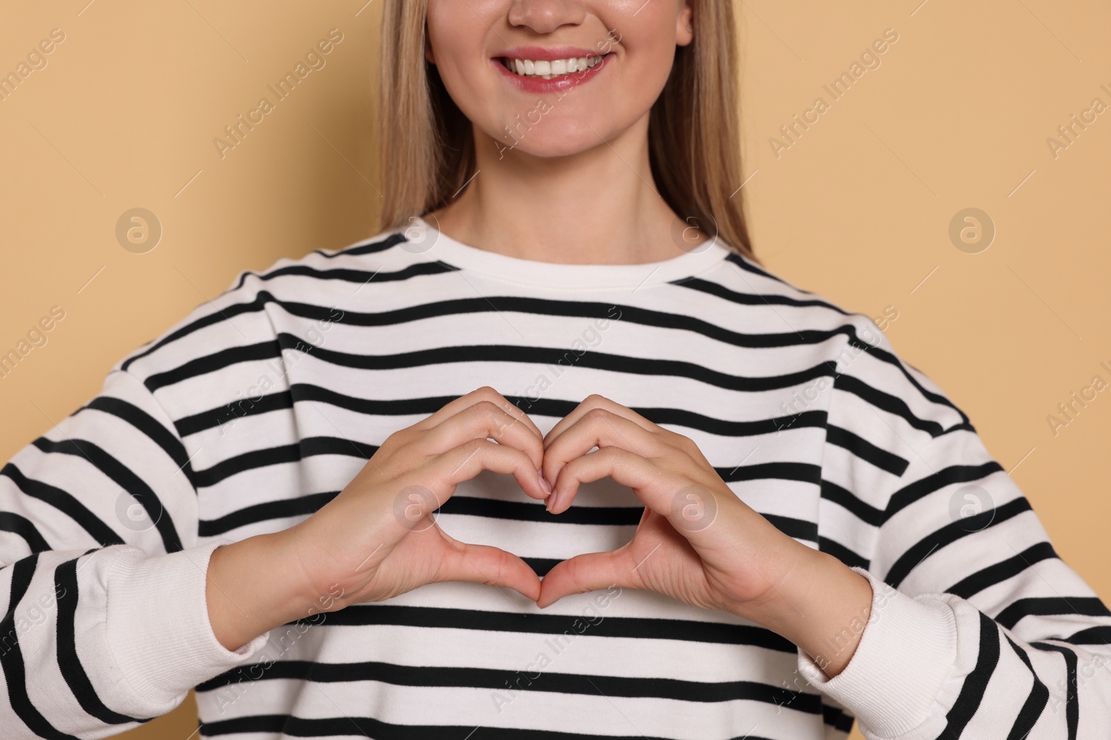 Photo of Happy volunteer making heart with her hands on beige background, closeup