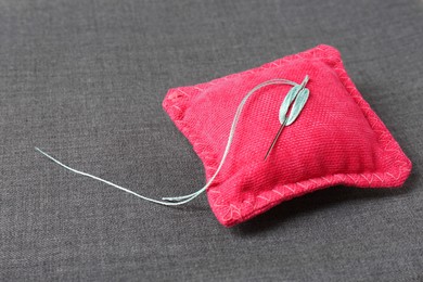 Photo of Pink cushion with needle and thread on grey fabric. Space for text