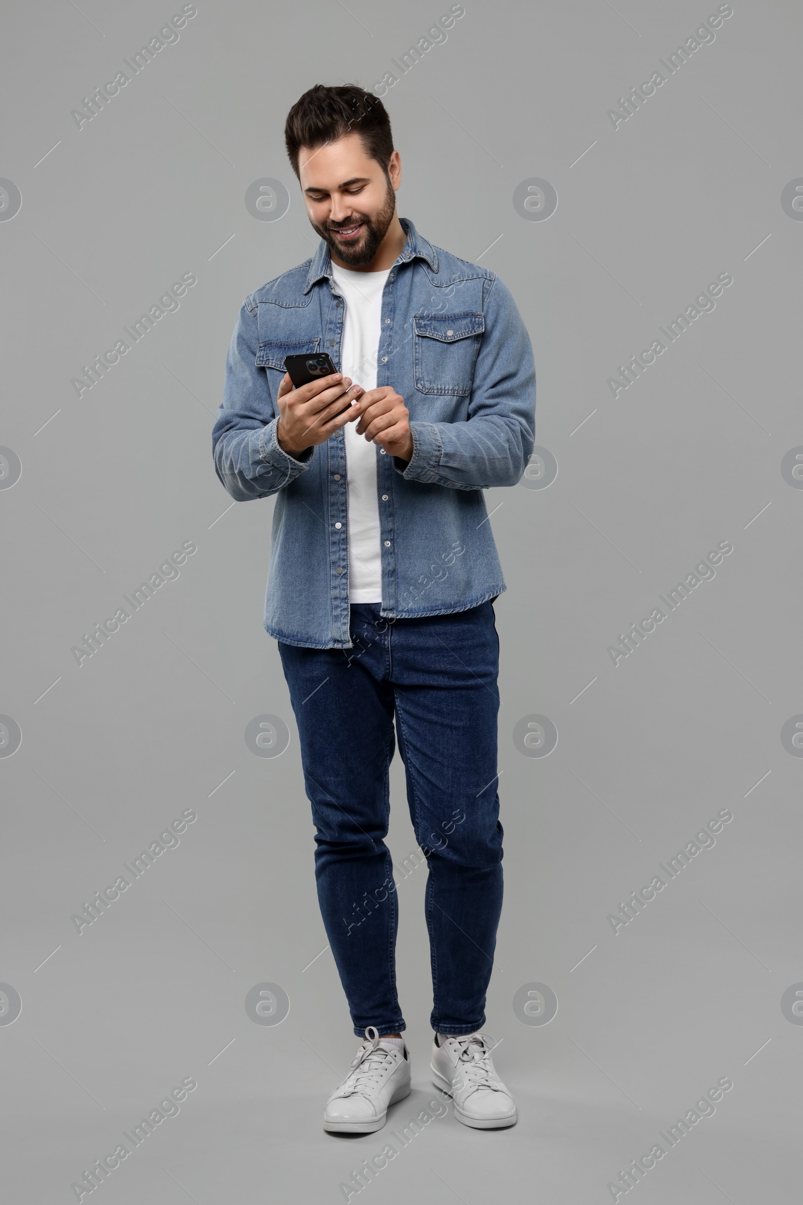 Photo of Happy young man using smartphone on grey background