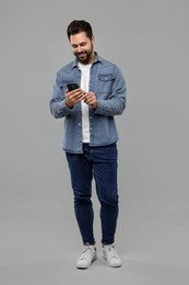 Happy young man using smartphone on grey background