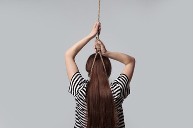 Photo of Woman with rope noose on neck against light grey background, back view