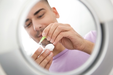 Photo of Mirror reflection of young man taking contact lens from container