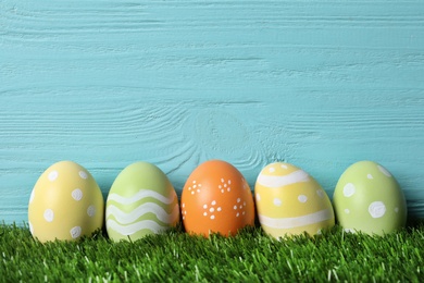 Colorful painted Easter eggs on green grass against wooden background, space for text