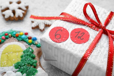 Photo of Saint Nicholas Day. Wrapped gift box with date December 6 and gingerbread cookies on snow, closeup