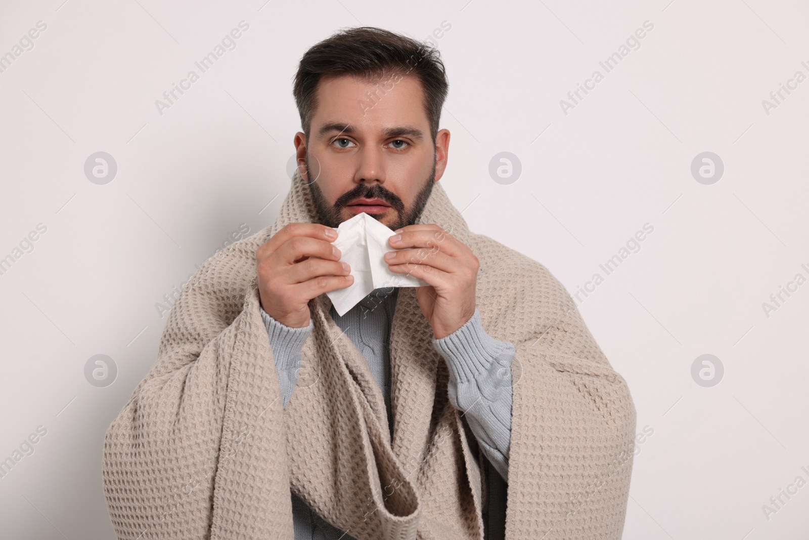 Photo of Sick man wrapped in blanket with tissue on light grey background. Cold symptoms