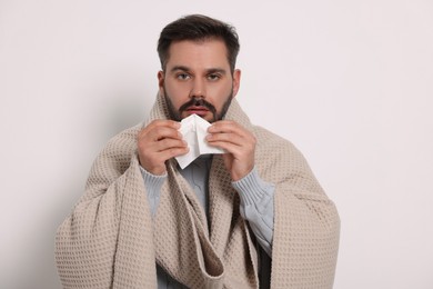 Photo of Sick man wrapped in blanket with tissue on light grey background. Cold symptoms