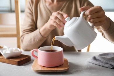 Woman pouring tea into ceramic cup at table, closeup