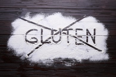 Photo of Crossed out word Gluten written with flour on dark wooden table, top view