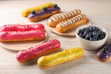 Photo of Different tasty glazed eclairs and blueberries on light wooden table, closeup