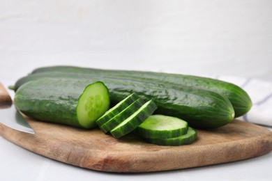 Fresh whole and cut cucumbers on white table, closeup