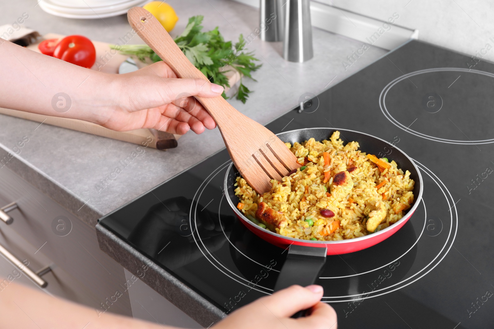 Photo of Woman frying rice with meat and vegetables on induction stove in kitchen, closeup