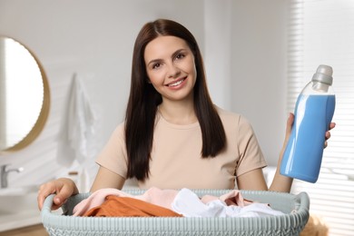 Photo of Woman holding fabric softener and basket with dirty clothes in bathroom